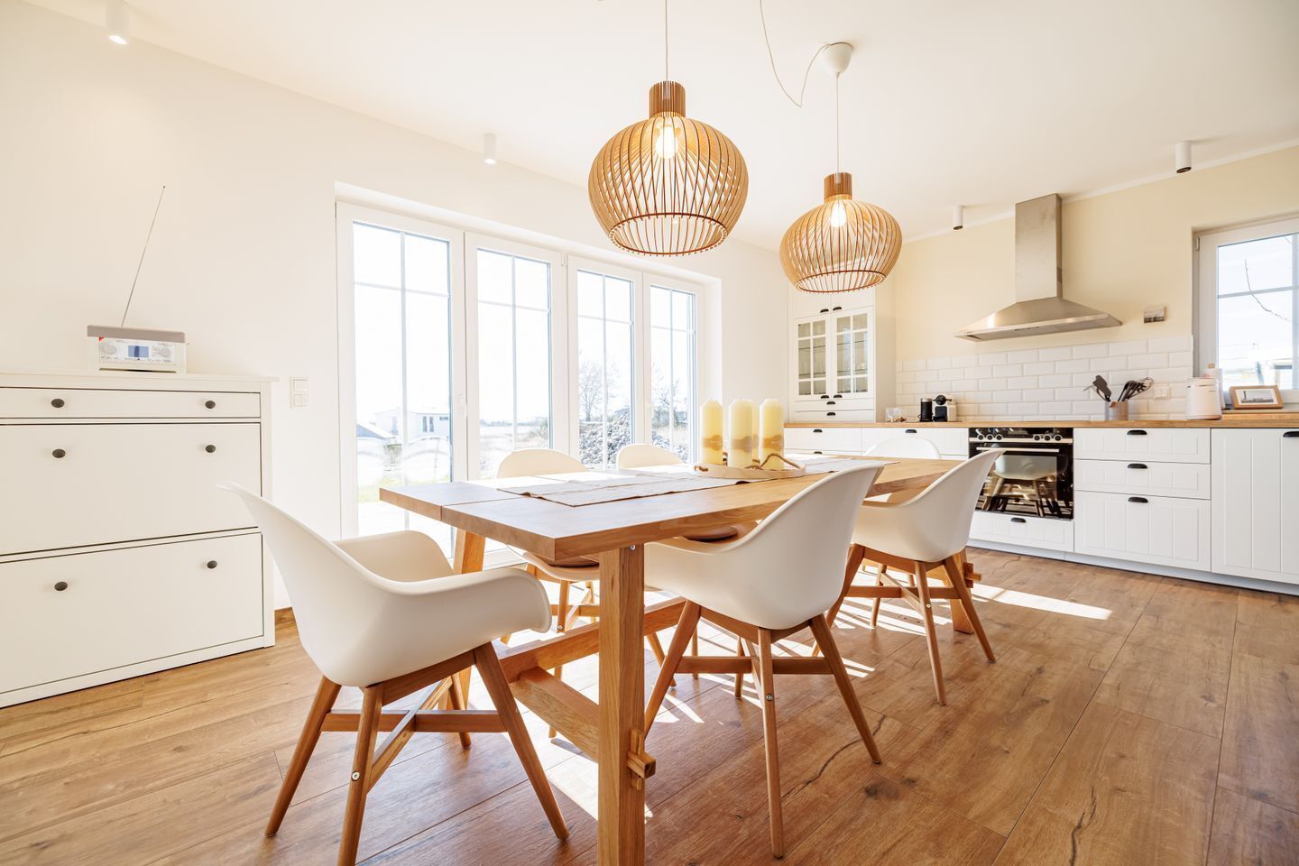 A modern kitchen with white cabinets, a wooden dining table, and pendant lights.