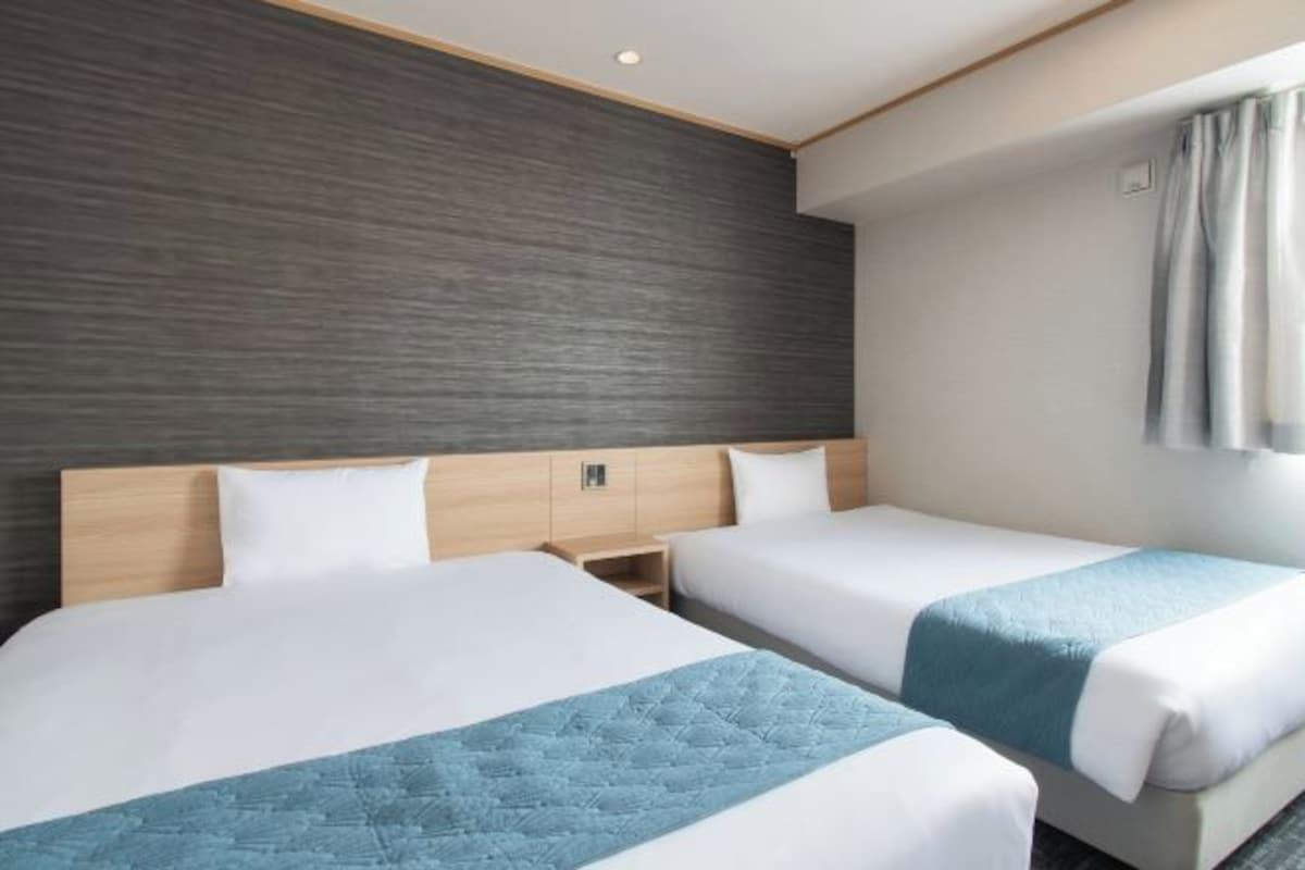 Une chambre d’hôtel avec deux lits, une tête de lit en bois, un mur de couleur sombre et une fenêtre avec des rideaux.