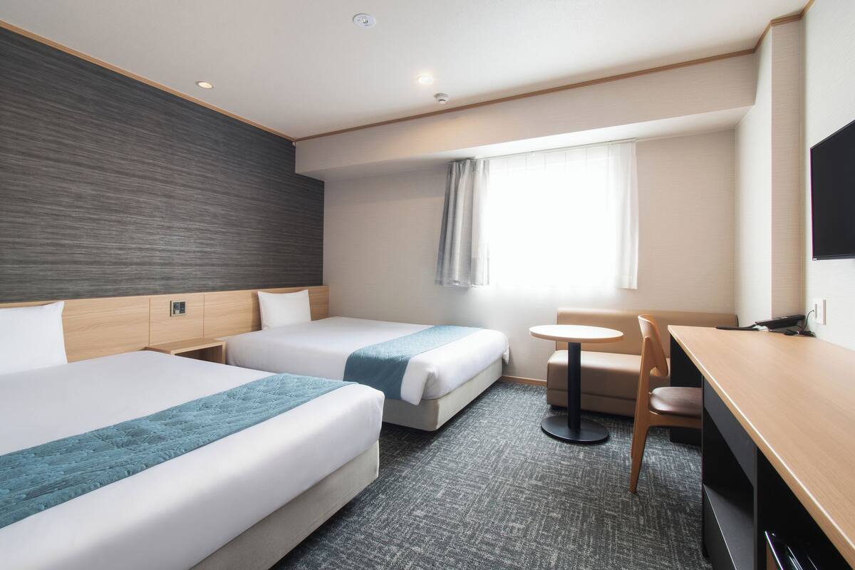 A hotel room with two beds, a desk, a chair, and a small table.
