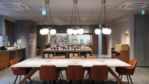 Un espace de salle à manger moderne, doté d’une grande table rectangulaire, de six chaises et de luminaires suspendus.