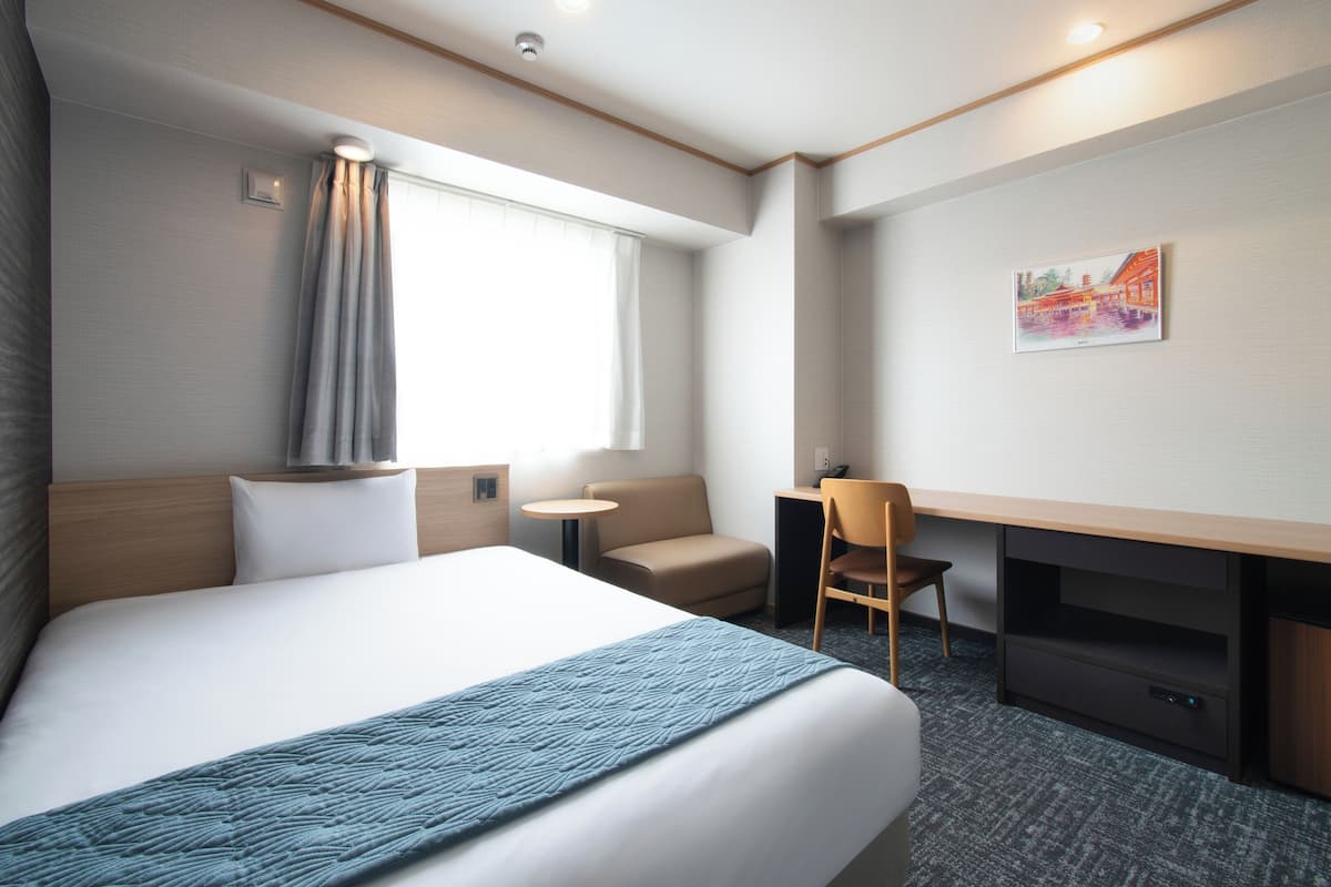 A hotel room with a large bed, a desk, a chair, a small table, and a painting on the wall.