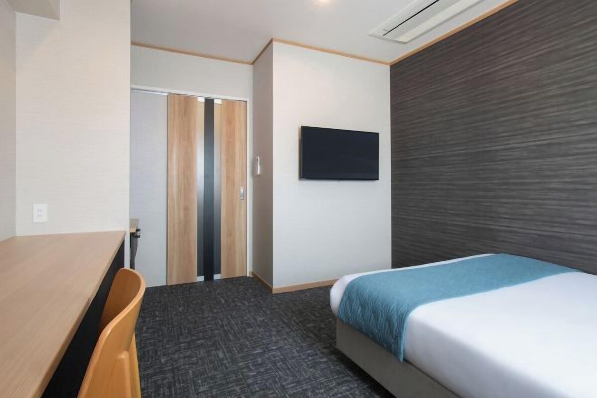 A hotel room with a bed, a desk, a chair, a wardrobe, and a television.
