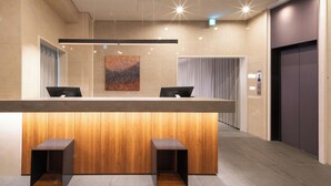Un comptoir d’accueil avec un panneau décoratif en bois, deux chaises noires, un luminaire moderne et un grand tableau abstrait accroché au mur.