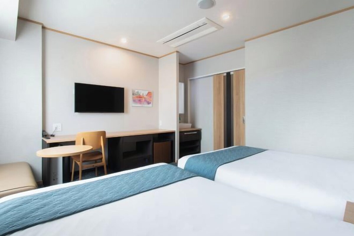 A hotel room with a bed, a desk, a chair, and a television.