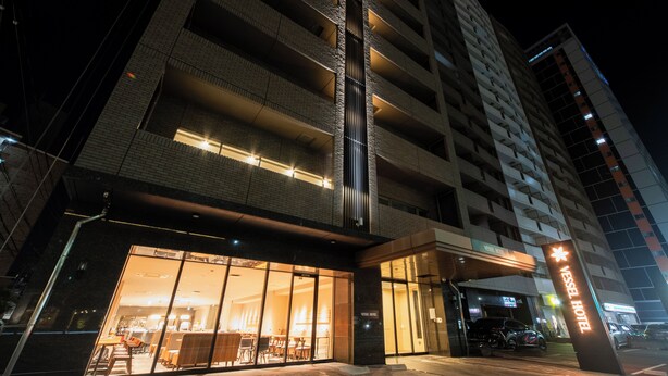 L’entrée d’un hôtel avec une façade en verre, une bande lumineuse verticale et une enseigne indiquant « Vessel Hotel ».