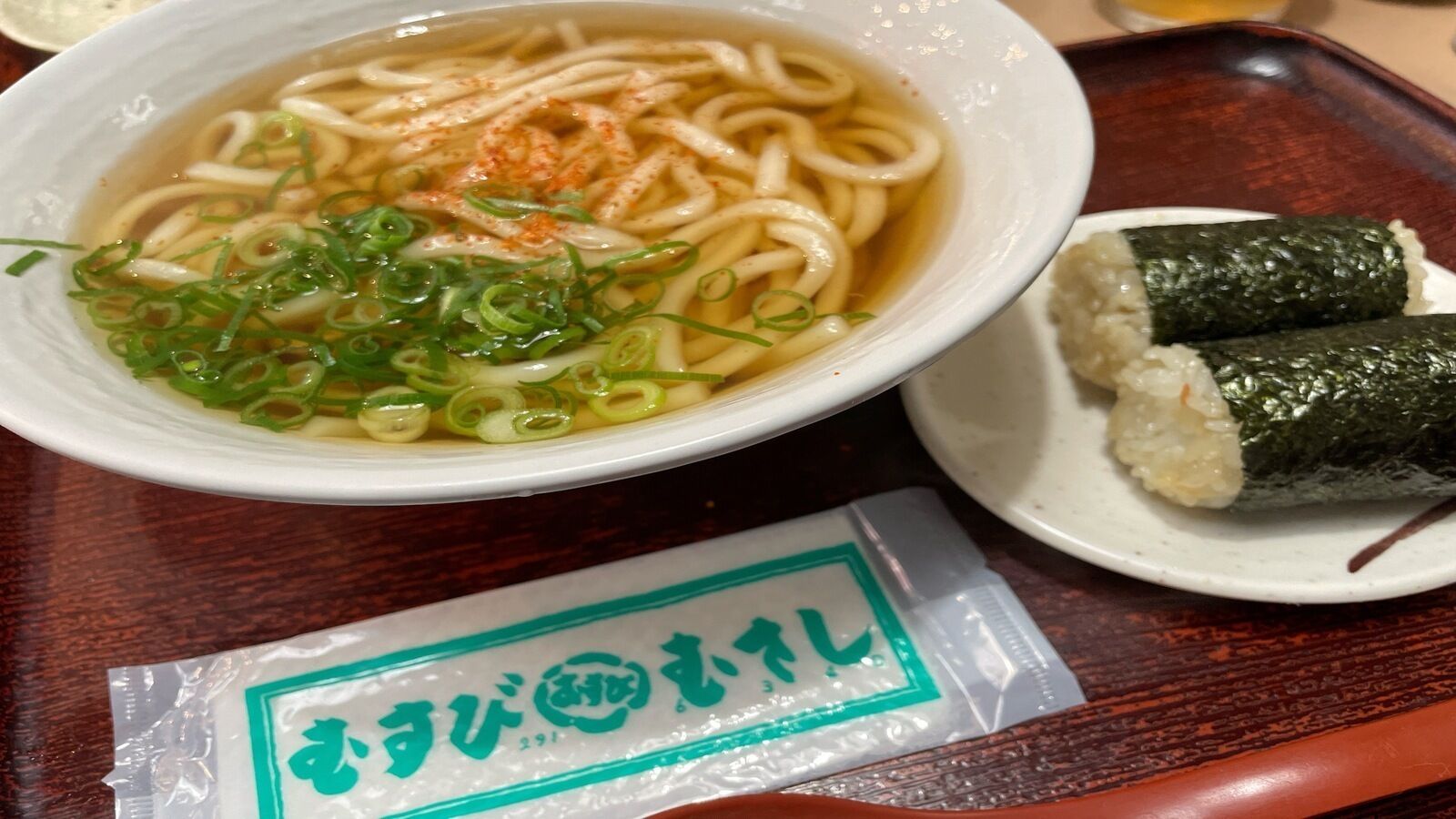 Un bol de ramen amb ceba verda i un paquet de wasabi sobre un plat.