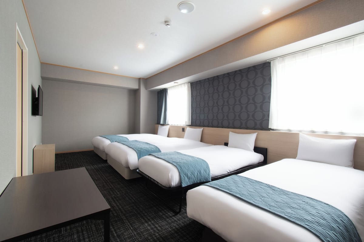 A hotel room with three beds, a flat-screen TV, a small table, and a window with a view.