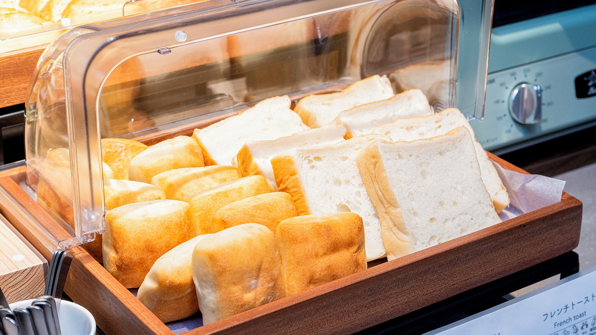 Un bufé con diferentes tipos de pan, incluyendo baguettes y bollos, presentado en una bandeja de madera.