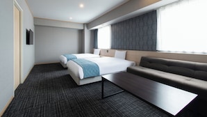 Une chambre d’hôtel moderne avec un grand lit, un canapé, une petite table et une fenêtre agrémentée de rideaux à motifs.