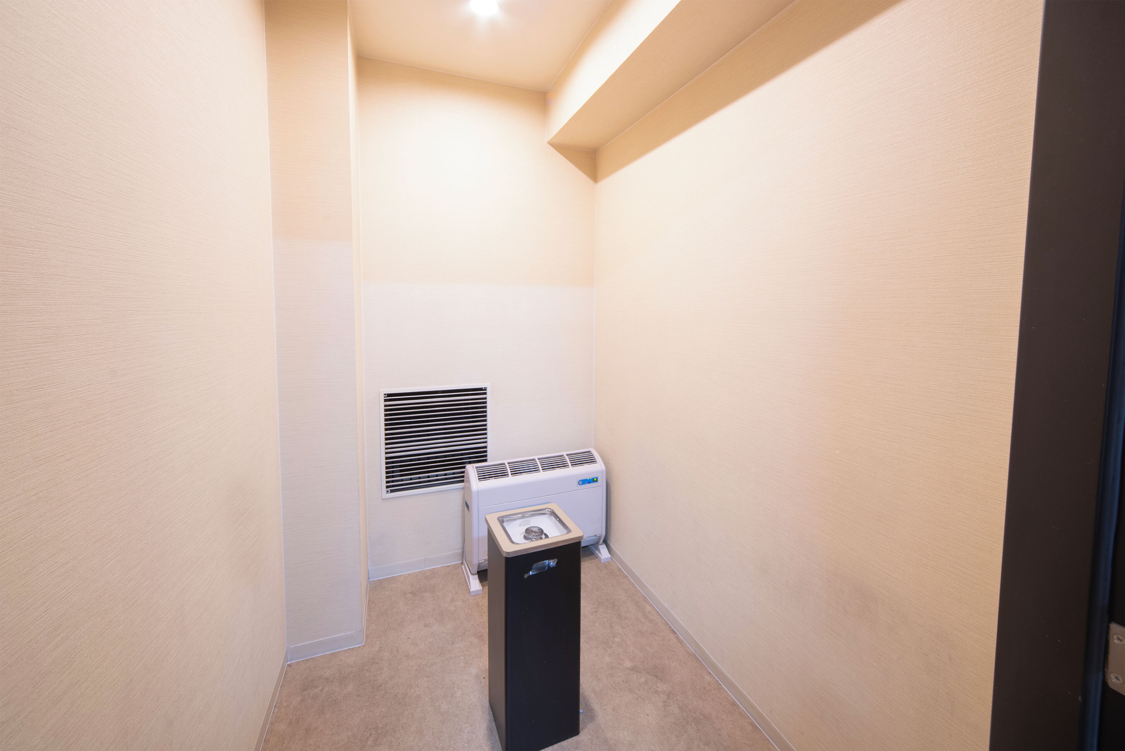 Um quarto pequeno e estreito, com paredes bege, um ar condicionado branco e um aquecedor preto.