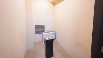 Um quarto pequeno e estreito, com paredes bege, um ar condicionado branco e um aquecedor preto.