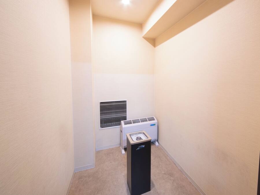 Um quarto pequeno e estreito, com paredes bege, um ar condicionado branco e um aquecedor preto.
