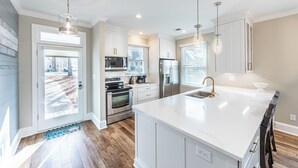 A modern kitchen with white cabinets, stainless steel appliances, and a large island with a sink. - 3 BR/4BA with ADDITIONAL Kids bunk room. (Greensboro)