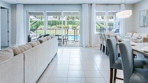 Un salon moderne doté d’un grand canapé, d’un coin repas avec des chaises et offrant une vue sur une piscine et un espace verdoyant.