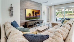 Un salon moderne avec un grand téléviseur à écran plat, une table basse en bois et un canapé beige.