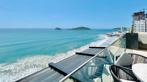 A balcony with a glass railing overlooking a beach with clear blue waters and a distant island. - The O  (Mazatlán)