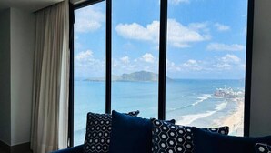 A room with a large window offering a view of the ocean and a beach. - The O  (Mazatlán)