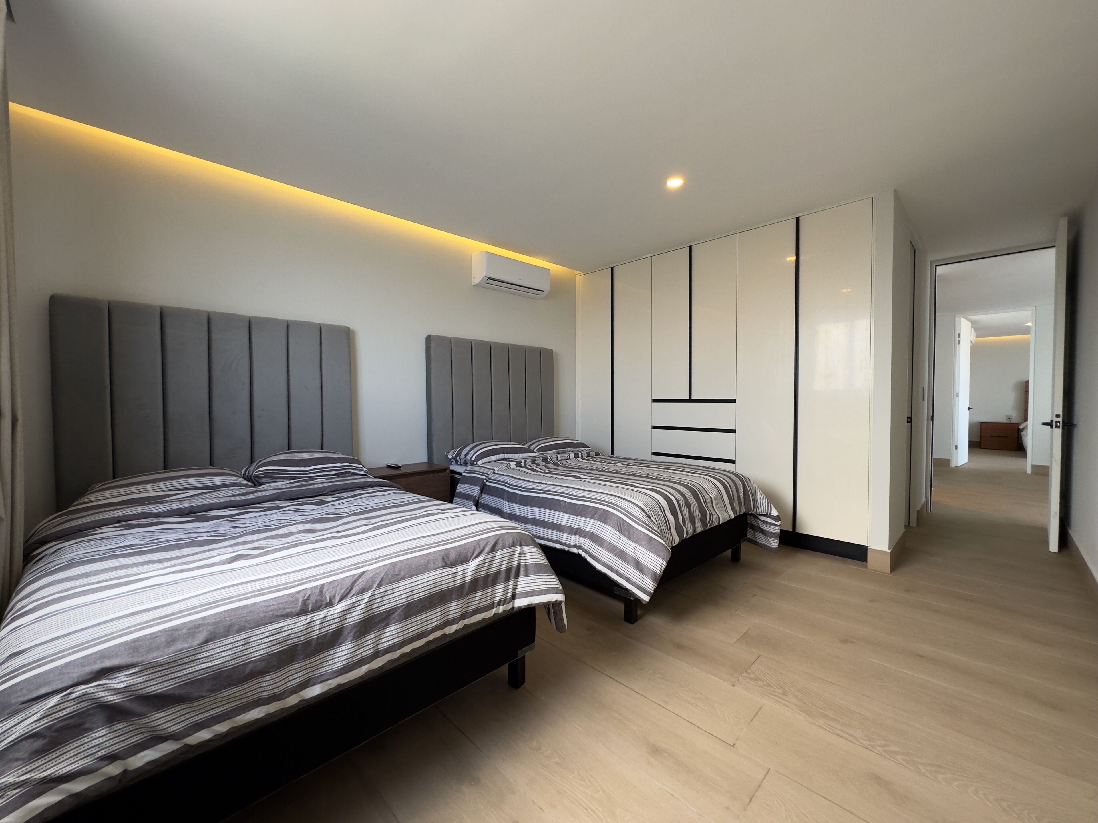 Een moderne slaapkamer met twee bedden, een garderobe en een gang naar een andere kamer.