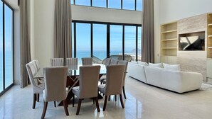 A spacious living area with a large window overlooking the sea, a white sofa, and a dining table with chairs. - The O  (Mazatlán)