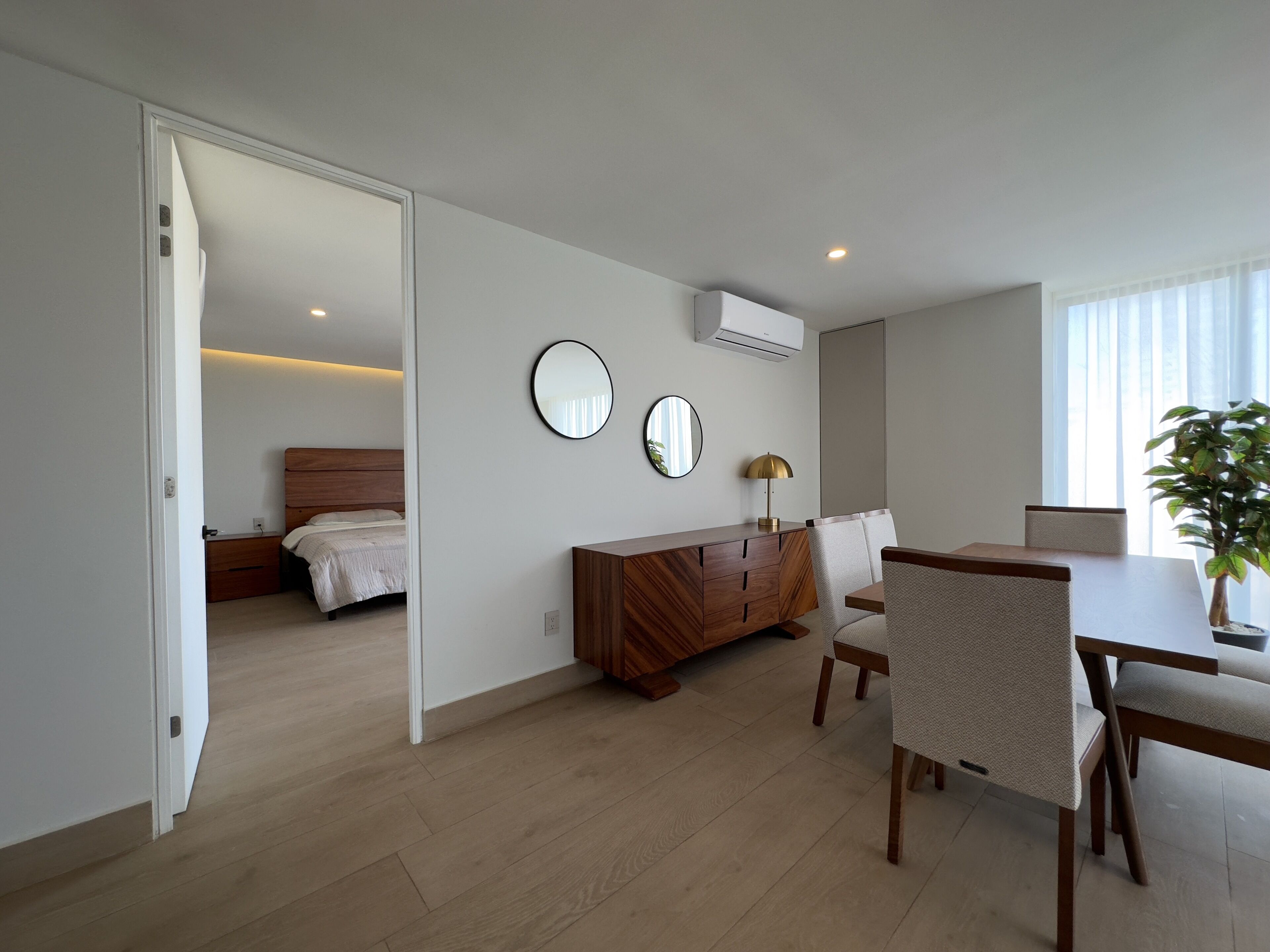 A modern hotel room with a wooden bed, a desk with a chair, a mirror, and a potted plant.