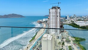 A high-rise building with a construction crane, overlooking a coastal city with a beach and a river. - The O  (Mazatlán)