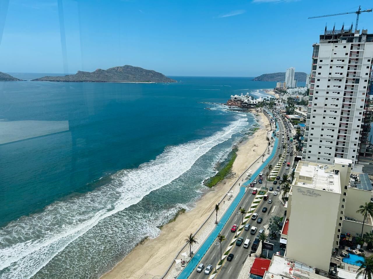 A coastal cityscape with a beach, a road parallel to the shore, and a high-rise building with a sign that reads "Don Palacios."