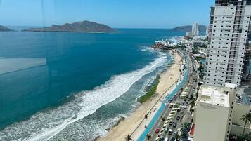 A coastal cityscape with a beach, a road parallel to the shore, and a high-rise building with a sign that reads "Don Palacios."