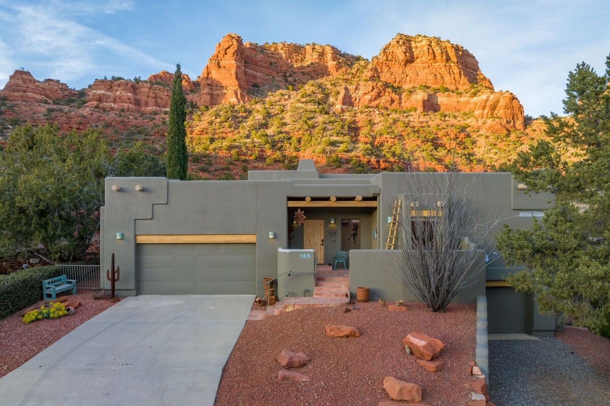 A modern building with a flat roof, a garage, and a patio area with red rocks and a cactus.