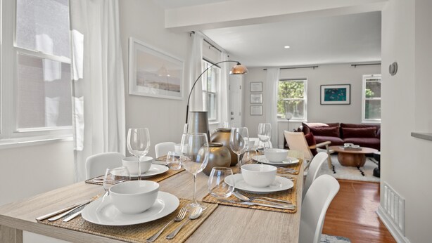 Un coin repas avec une table en bois dressée pour le repas, entourée de chaises blanches.