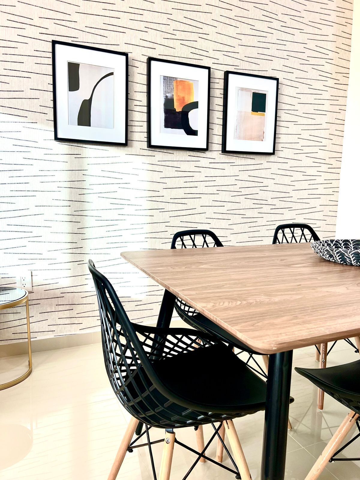 A dining area with a wooden table and black chairs with a geometric design. There are three framed abstract artworks on the wall.