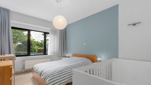 Una camera da letto con un letto, una culla, una finestra con tende, un termosifone e una lampada a sospensione.