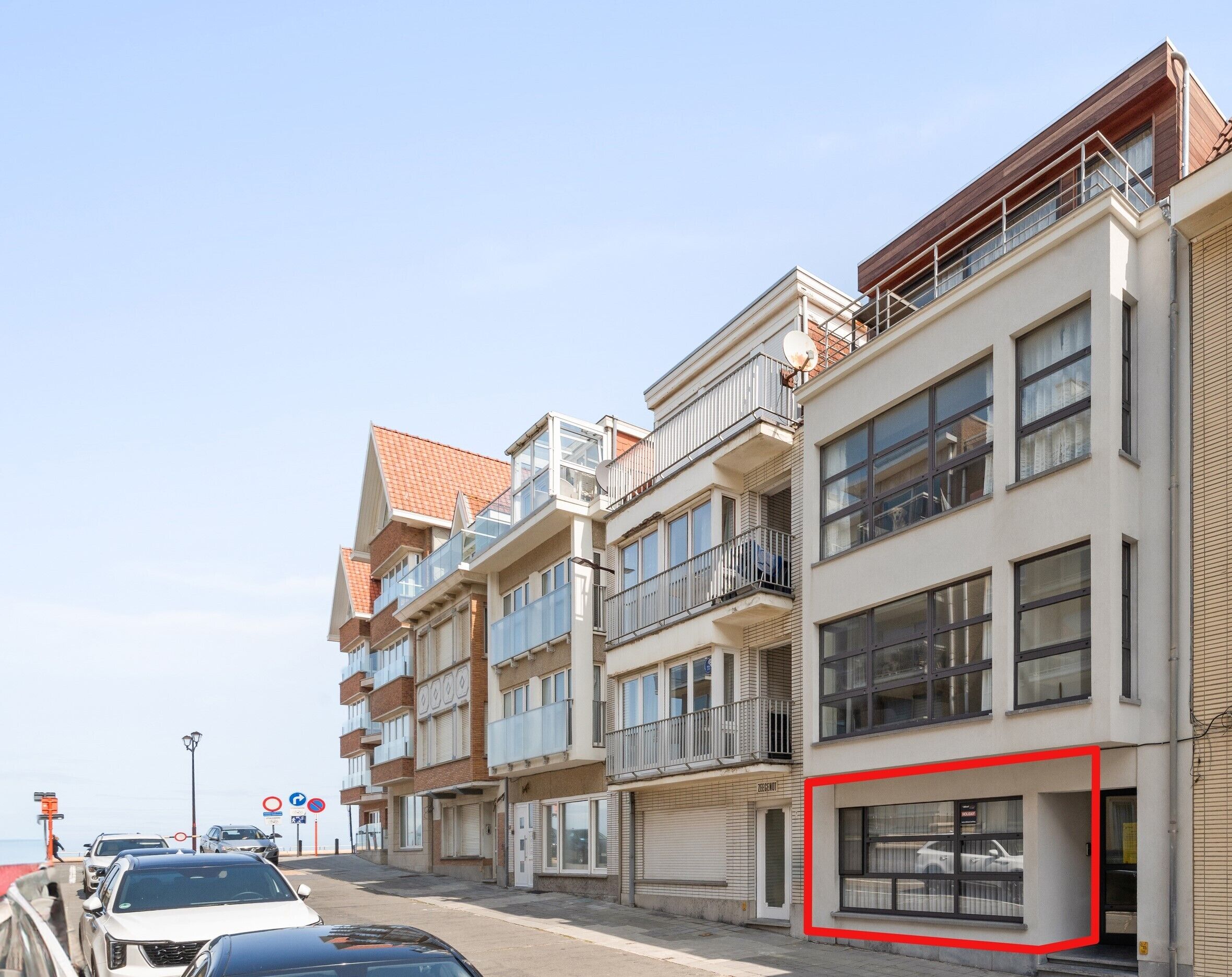 Une rangée d’immeubles modernes à plusieurs étages, dotés de balcons, un espace de stationnement et un ciel dégagé.