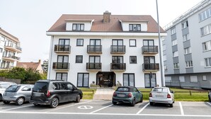 En flervåningsbostadsbyggnad med ett tak täckt av takpannor, balkonger och en parkeringsplats med flera bilar.