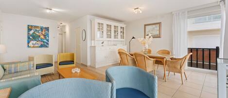 A modern living room with a sofa, chairs, a dining table, and a kitchen area with cabinets and a window.