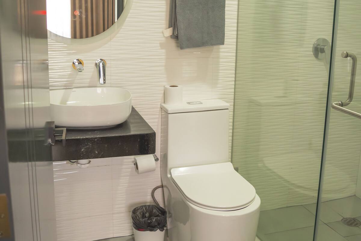 A modern bathroom with a round mirror, white sink, and glass shower enclosure.