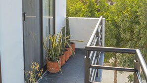 Un balcón con plantas en macetas, una puerta corredera de vidrio y una barandilla de metal.