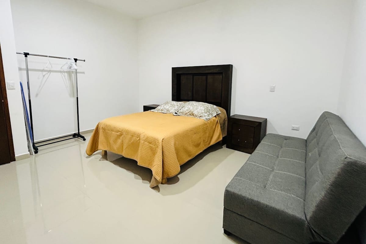 Un dormitorio con una cama, una mesita de noche, un sofá gris y un perchero.