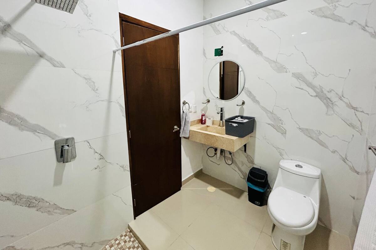 Un baño con pared de mármol, puerta de madera, lavabo con espejo, inodoro y ducha.