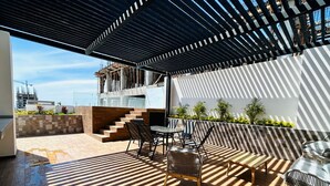 An outdoor patio with a wooden deck, a table with chairs, and a staircase leading to an upper level. - Flamingos (Mazatlán)