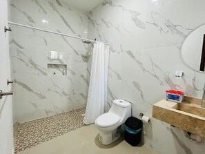 A bathroom with a toilet, a shower curtain, a sink with a soap dispenser, and a trash bin.