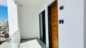 A balcony with a white wall, a wooden door, and a glass door. - Flamingos (Mazatlán)