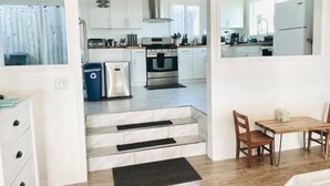 A modern kitchen with white cabinets, stainless steel appliances, and a wooden dining area with a table and chairs. - Water’s Edge - Ocean views, Private hot tub (Bodega Bay)