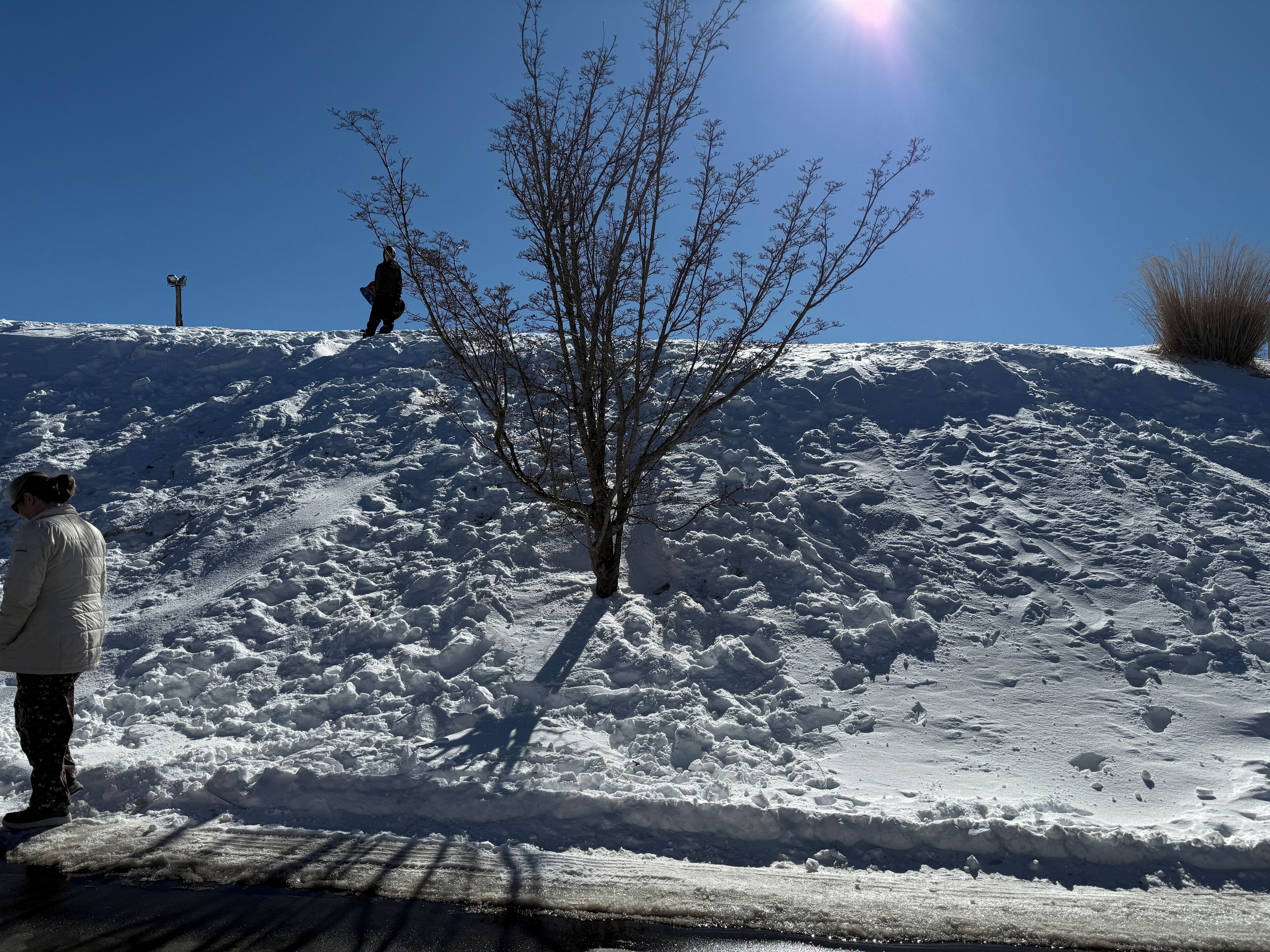 Une colline enneigée, avec une personne debout à son pied.