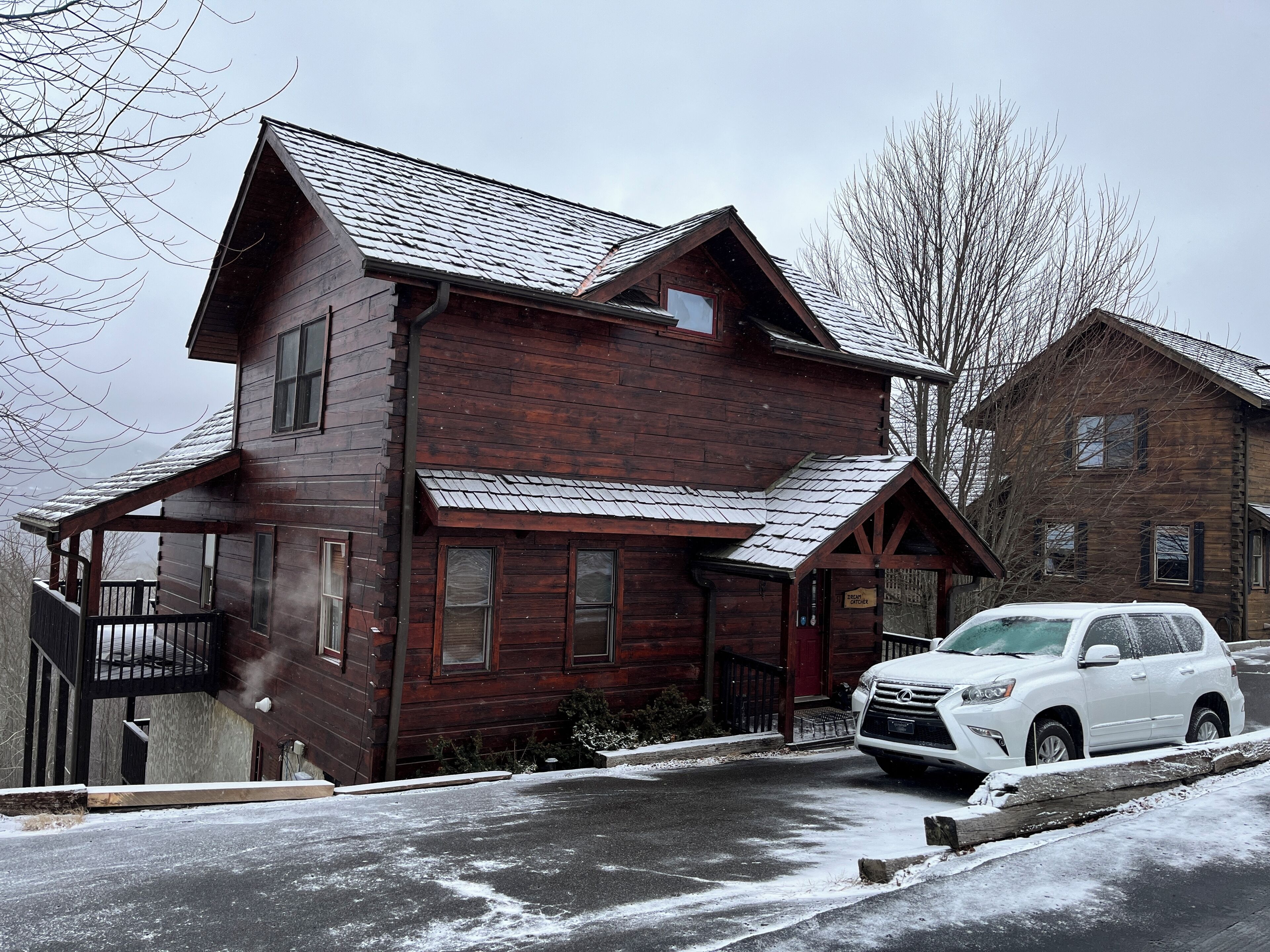 A two-story wooden cabin with a covered porch and a car parked in front.