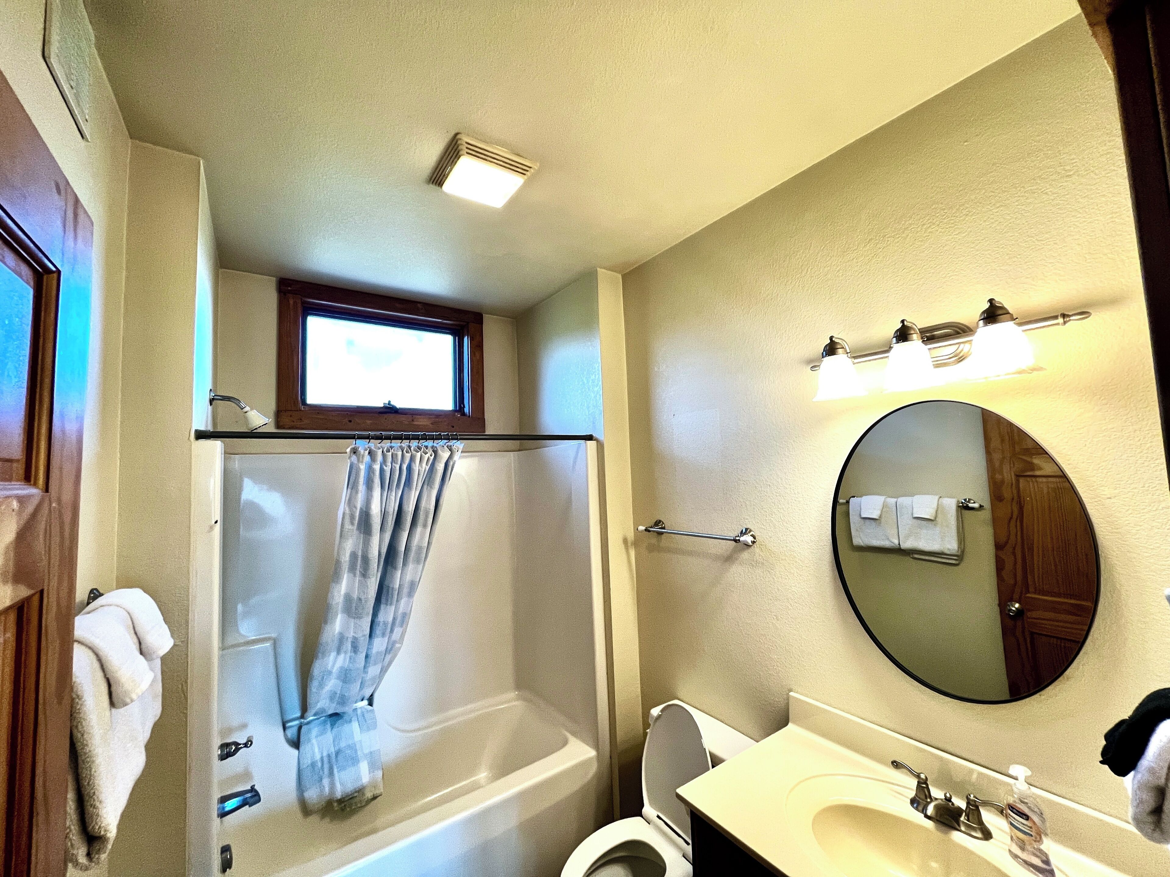 Een badkamer met een bad, toilet, wastafel en een raam boven de douche.
