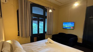 Hotelkamer met een bed, een televisie, een plafondventilator en uitzicht op het balkon.