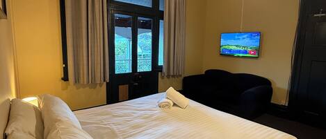 A hotel room with a bed, a TV, a ceiling fan, and a view of the outside balcony.