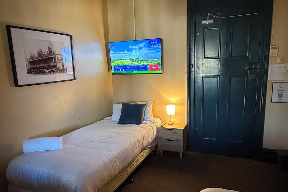 Una habitación de hotel con una cama, una mesita de noche con lámpara, un televisor en la pared y una puerta.