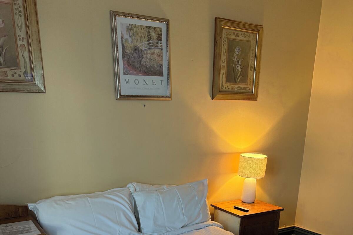 Una cama bien tendida con sábanas blancas, una toalla enrollada y una mesita de noche con una lámpara.