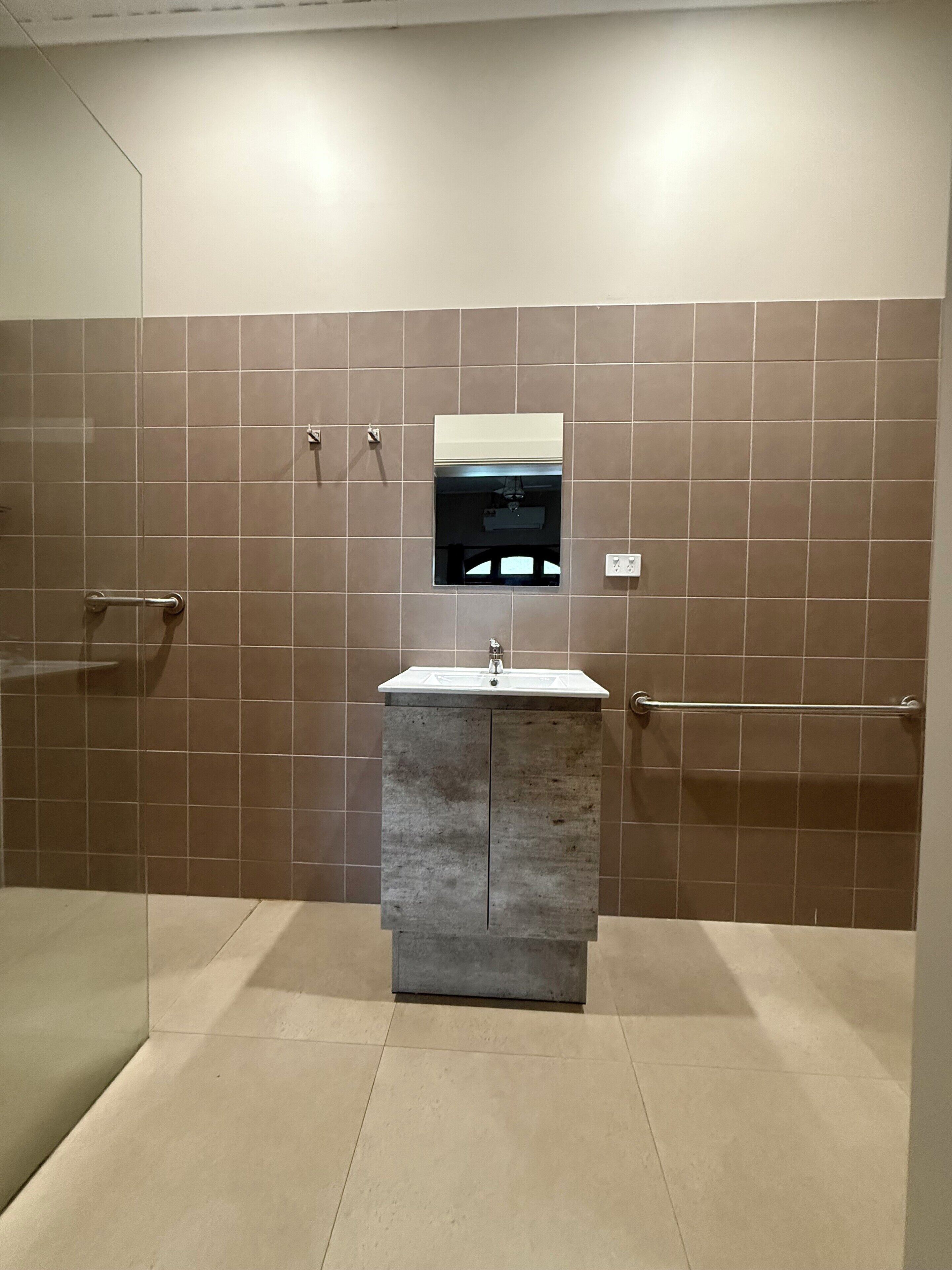 A bathroom with a shower, a sink with a mirror, and tiled walls.